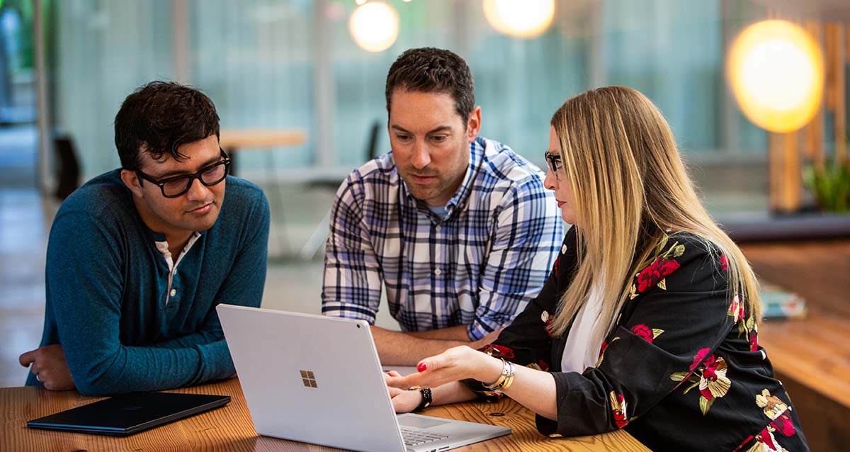 Drei Personen blicken gemeinsam auf ein Surface Laptop.