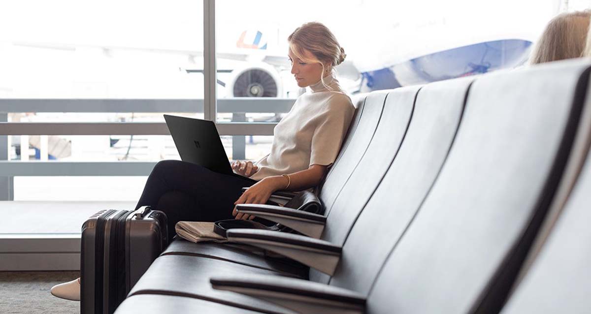 Eine Frau am Flughafen-Gate mir einem Surface Laptop vor ihr.