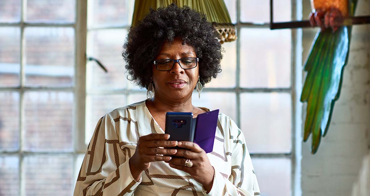 Eine Frau steht vor einem Fenster und blickt auf ihr Smartphone.
