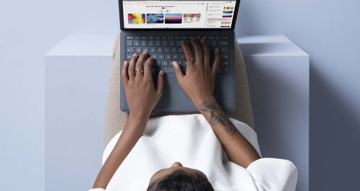 Mann sitzt und tippt auf seinem Surface Laptop. Eine Website ist auf dem Bildschirm zu erkennen.
