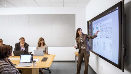 Woman standing in a meeting room showing others grpahs on a screen