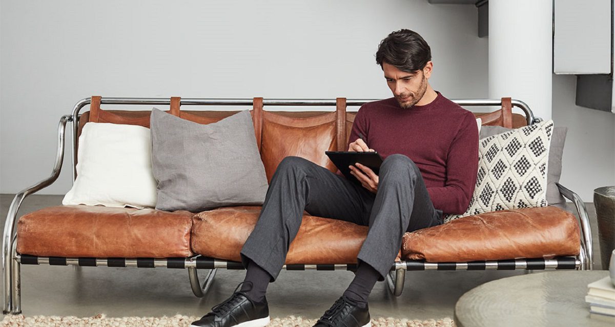 Man sitting on couch and using a stylus to write on a handheld tablet.