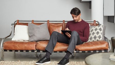 Man sitting on couch and using a stylus to write on a handheld tablet.