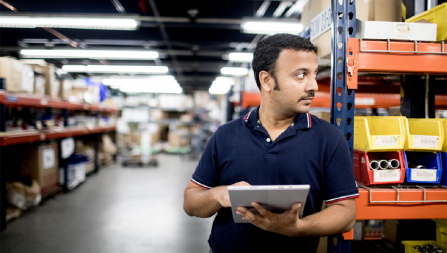 Man standing among warehouse shelves holding a tablet.