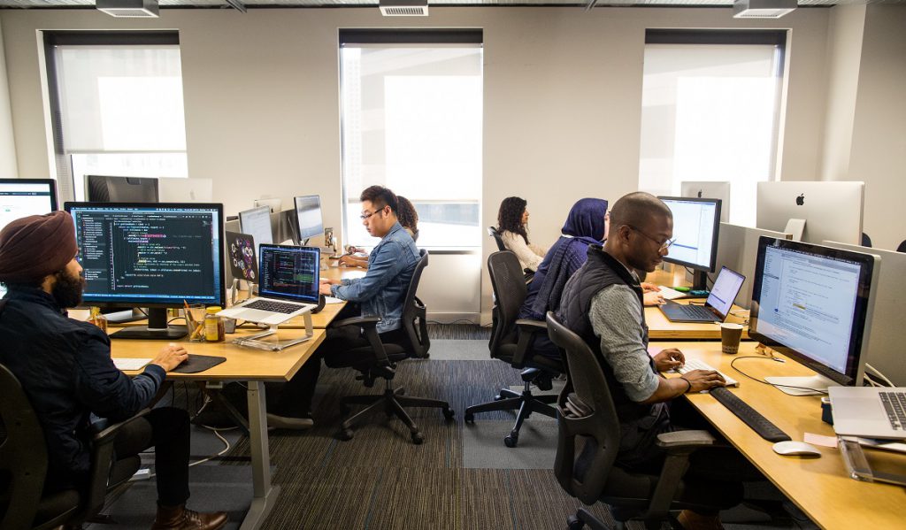Six developers working at their individual workstations in an office
