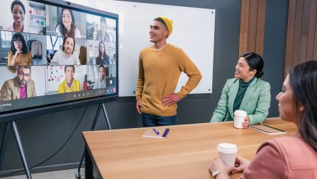 Group of coworkers in a conference having a video call with nine other people on a large screen