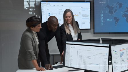 Three cybersecurity professionals reviewing information on various screens in an office