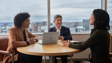 Three people meeting at a conference table with a Surface Laptop Go 2. No screen showing.