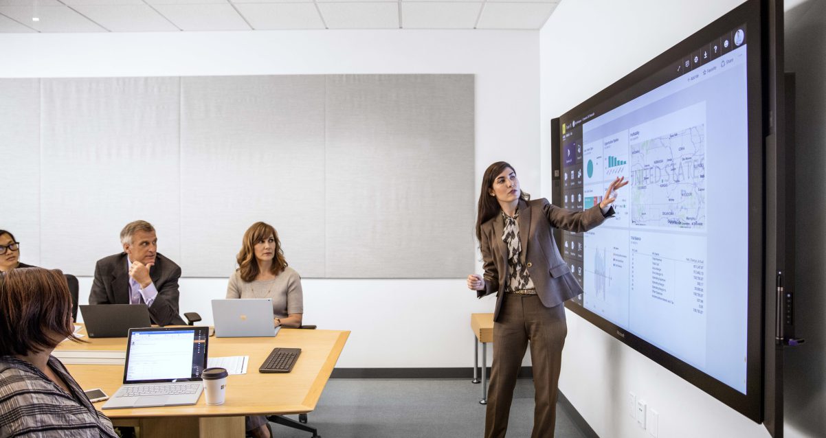 Woman standing in a meeting room showing others grpahs on a screen