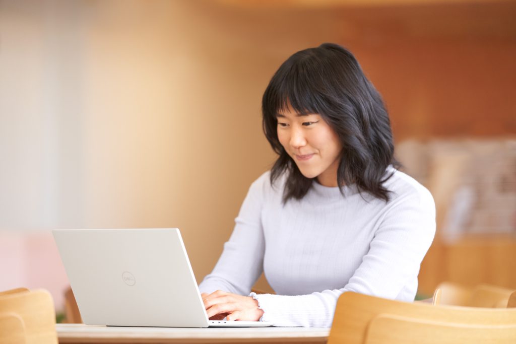 Woman sitting at a desk in front of her laptop and typing somehting while smiling.