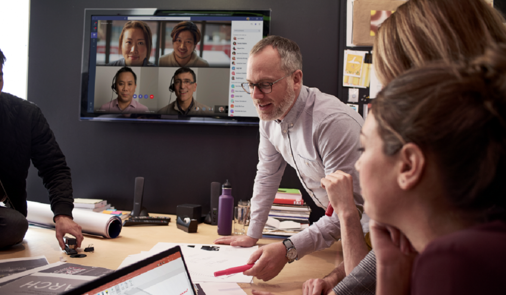 Team meeting in a conference room while videoconferencing with four other people on a large screen