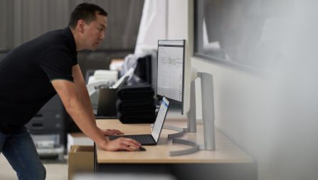 Man standing at desk where laptop is connected to two monitors