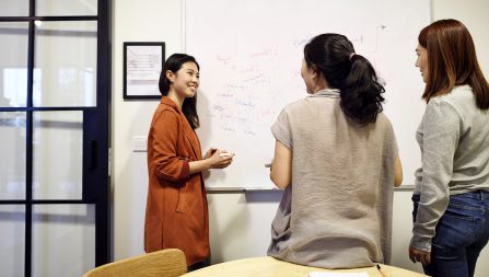 Three women in an office using a whiteboard to brainstorm