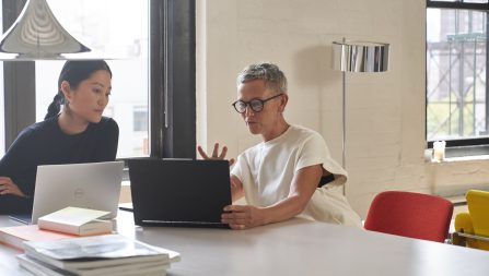 Two women at a desk with laptops open in conversation
