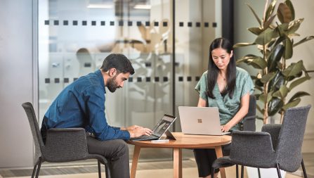 Man and woman collaborating in an office space, each with their own laptops