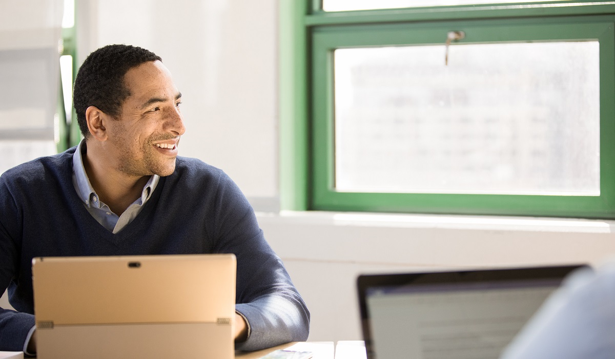 Smiling man sitting behind laptop in modern workspace
