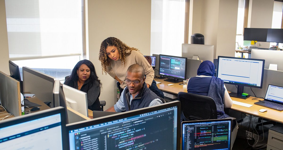 Three coworkers looking at code on a computer in their office