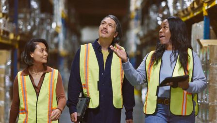 Three coworkers in construction vests walk through a warehouse