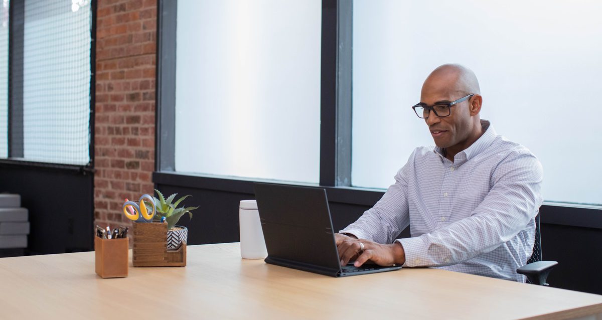 A professional man wearing glasses works at a conference table on his laptop